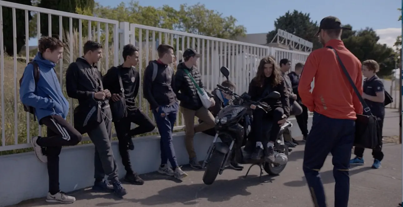 Group of students hanging out near a fence.