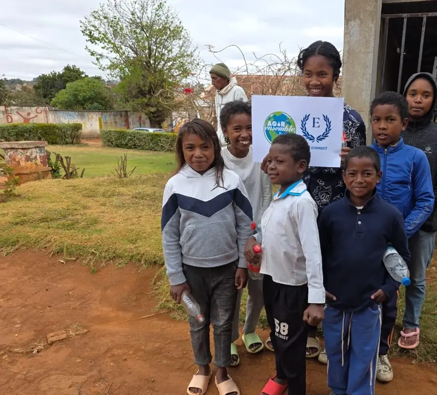 Des enfants tenant une pancarte, debout à l'extérieur, souriants.