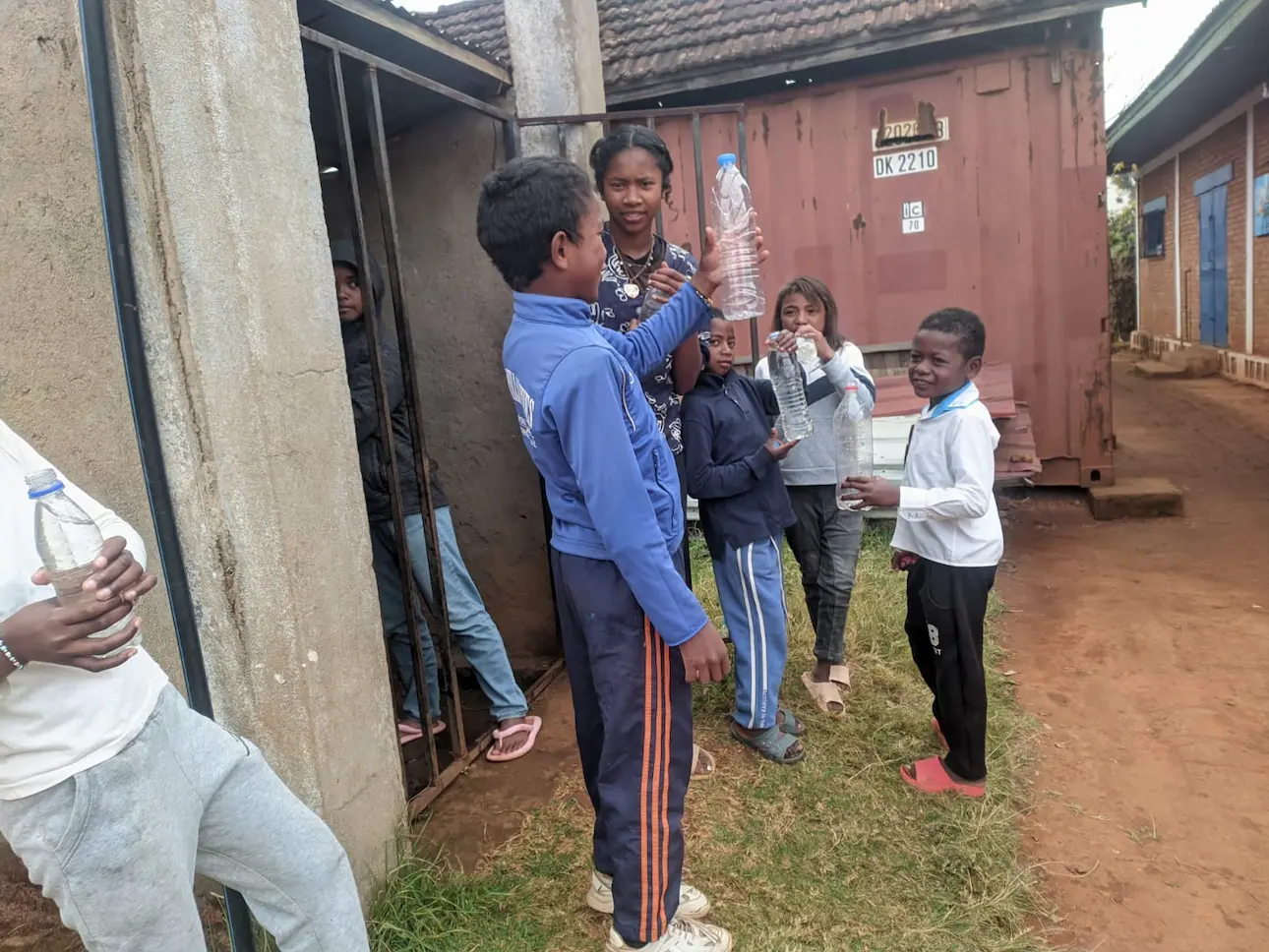 Des enfants tenant des bouteilles d'eau à l'extérieur d'un bâtiment.