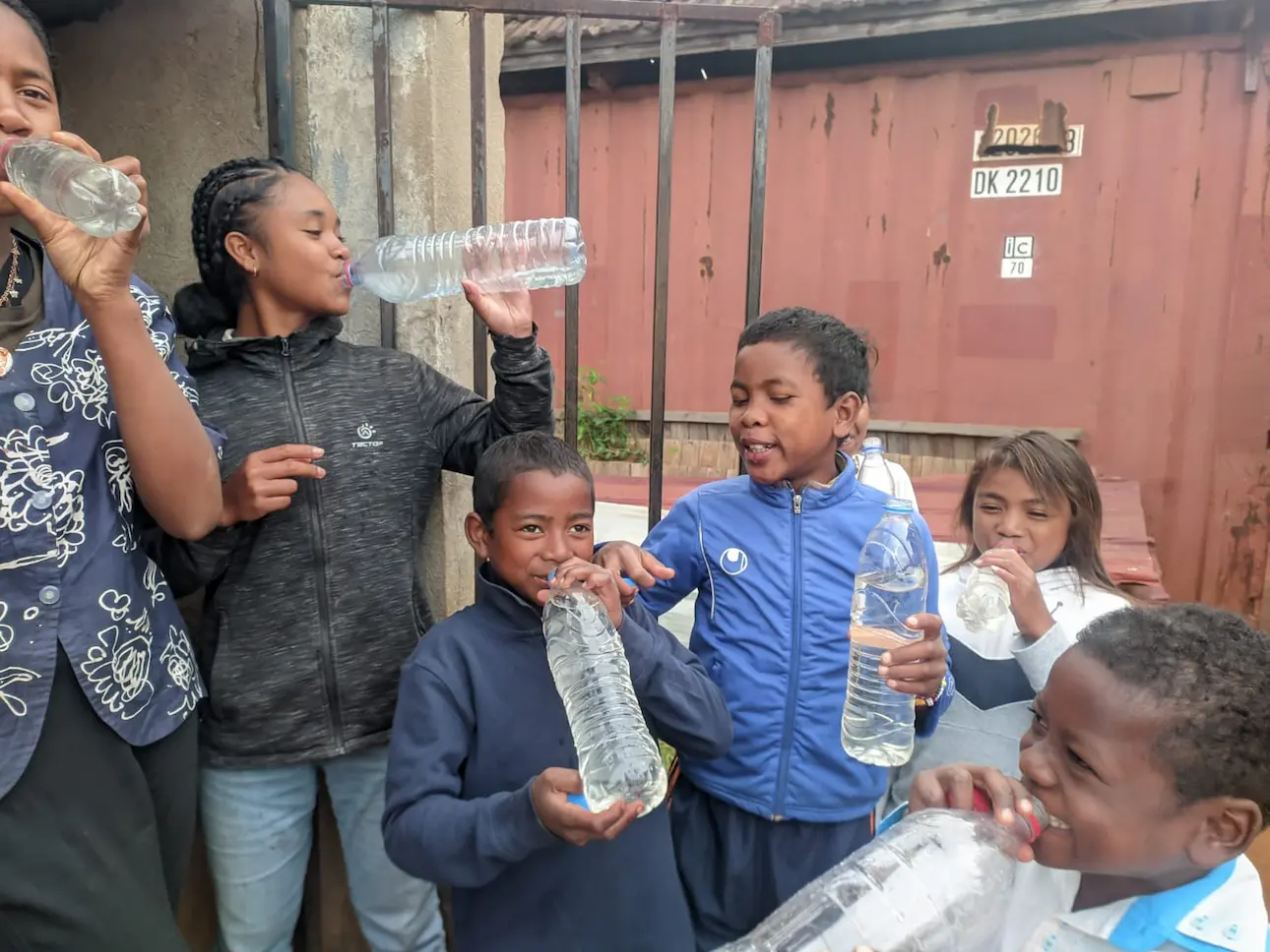 Des enfants boivent de l'eau dans des bouteilles en plastique à l'extérieur.